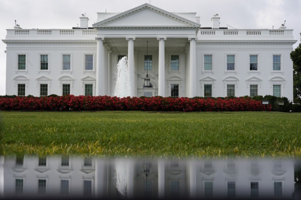 This photo shows the White House, including its reflection in a puddle in the foreground, on Sept. 3, 2022. In front of the White House are green grass and a fountain shooting water vertically into the air.