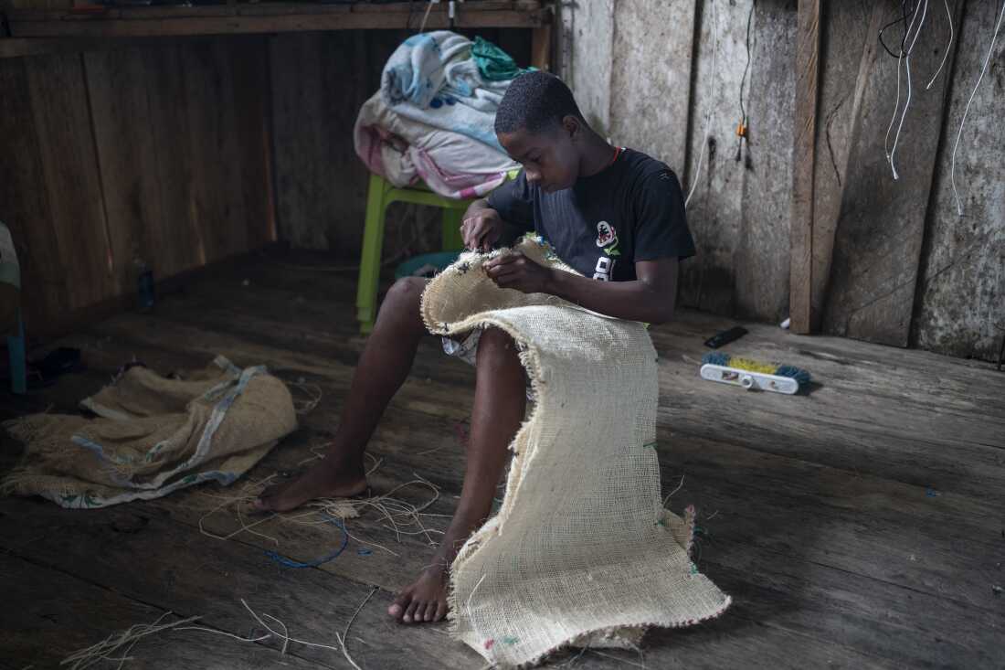 A boy designated as Manacillo, sews his costume for Holy Week, March 29, 2024, in Juntas, Buenaventura, Colombia. Photographer: Nathalia Angarita