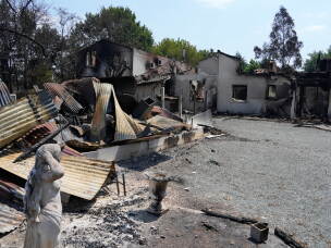 A statue stands in front of the remains of a house after wildfires raged in the village of Le Porge, on the Bay of Biscay, France, Monday, July 27, 2026.