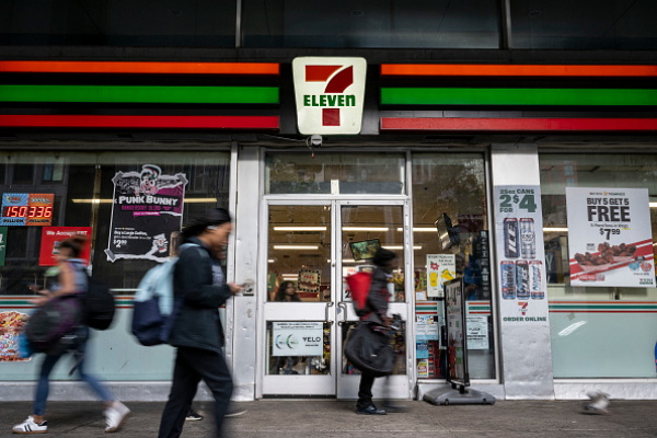 People walk past a 7-Eleven convenience store in New York City on Wednesday. The company plans to shut down 444 stores across North America to recoup costs lost to inflation, a drop in store traffic and declining cigarette sales.
