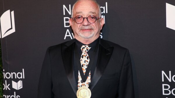  Author Rabih Alameddine wearing a black suit with a National Book Award around his neck.