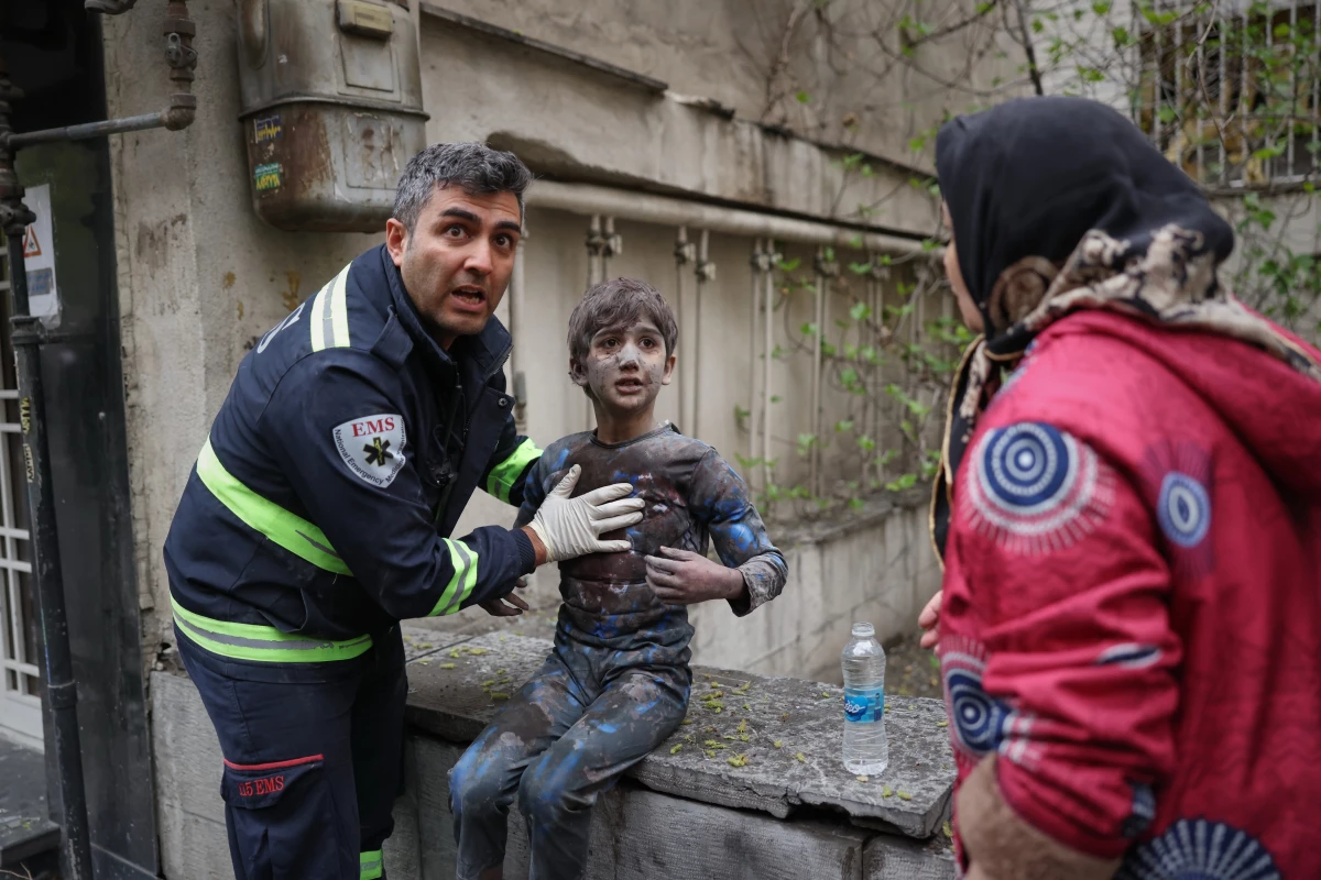 A first responder assists an injured boy following a strike that hit a residential building amid the U.S.-Israeli military campaign in Tehran, Iran, Saturday, March 28, 2026.