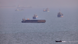 A small boat sails past cargo ships and other commercial vessels anchored in the Strait of Hormuz off Bandar Abbas, Iran, on Aug. 5.