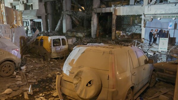 People inspect the site of a destroyed branch of Al-Qard Al-Hassan, a non-bank financial institution run by Hezbollah, which was hit by an Israeli airstrike in central Beirut. Debris and destroyed vans are amongst the rubble.