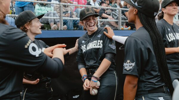 Brittany Apgar (from left), Maggie Foxx and Mo'ne Davis, of the Los Angeles Queens, joke around in the dugout. Their uniforms are dark gray and say "Los Angeles" across the front and "Inaugural Season" on the sleeve. 