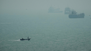 A motorboat travels past commercial vessels anchored amid haze in the Strait of Hormuz off Bandar Abbas, Iran, Monday, Sept. 7, 2026.