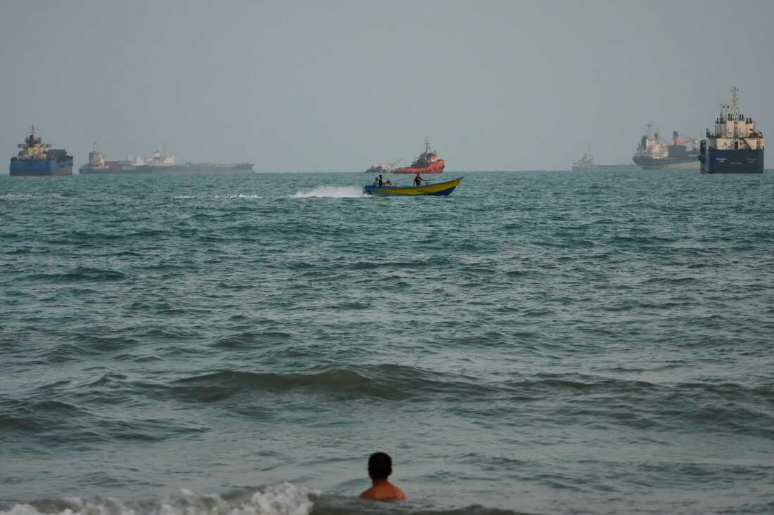A swimmer remains near the shore as a motorboat passes commercial vessels anchored in the Strait of Hormuz off Bandar Abbas, Iran,on Friday.