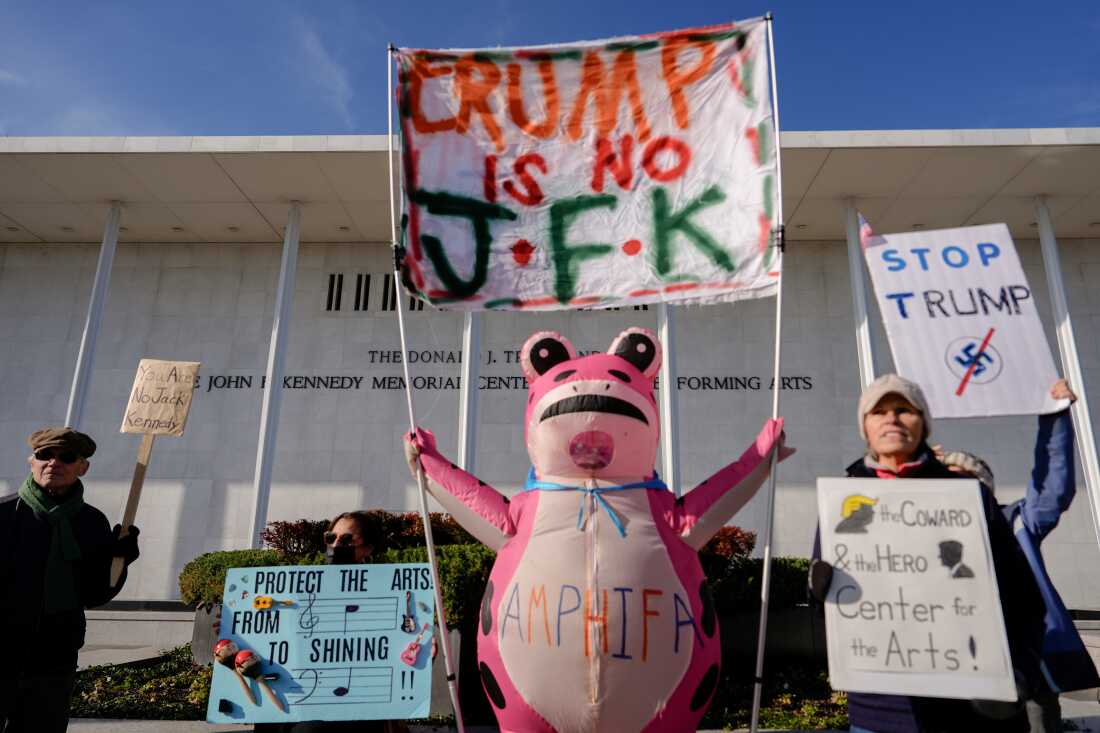 Protesters, including Nadine Siler of Waldorf, Maryland, dressed in a pink frog costume, hold signs at a designated protest point in front of the John F. Kennedy Memorial Center for the Performing Arts, a day after a Trump-appointed board voted to add President Donald Trump's name to the Kennedy Center, Saturday, Dec. 20, 2025, in Washington. (AP Photo/Julia Demaree Nikhinson)