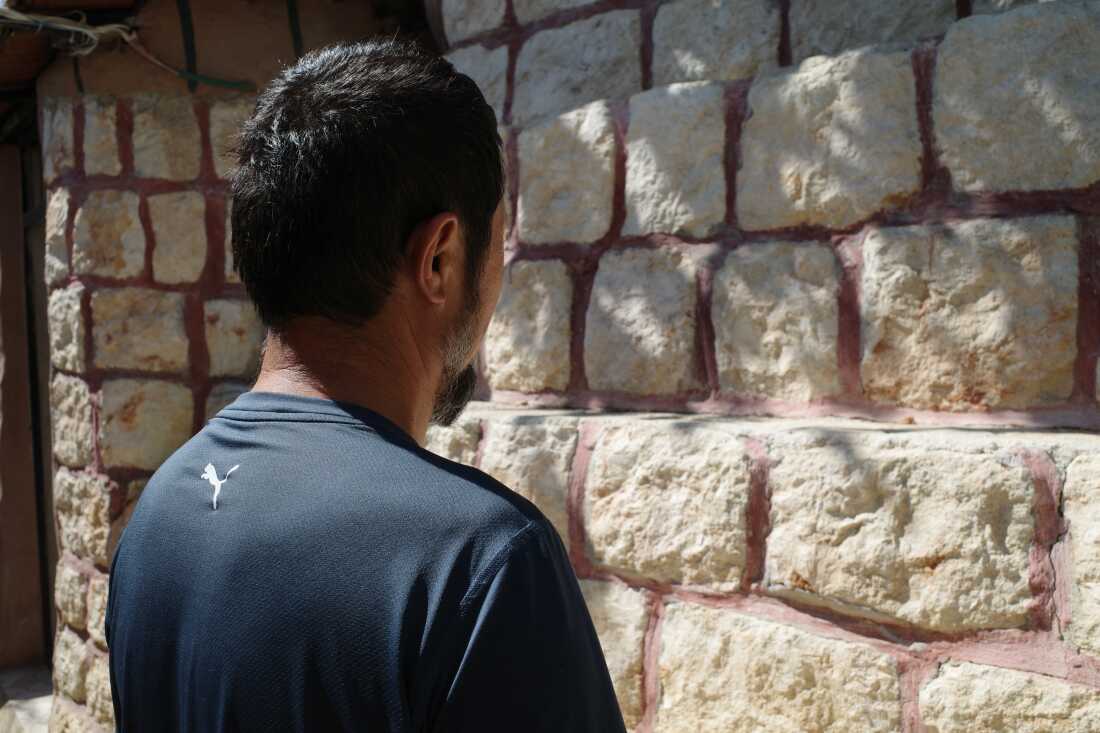 Photographed from the back, Nurmemet stands facing a structure made from stacked stones. He's wearing a navy blue synthetic top.