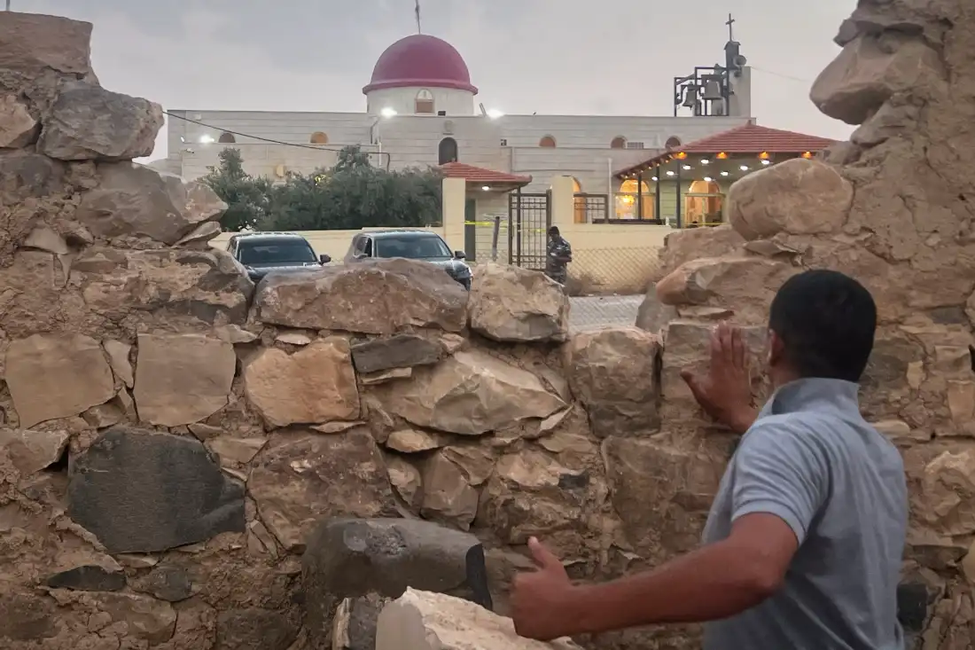A man looks through a gap in a stone wall toward a Greek Orthodox church where gunmen opened fire during a funeral hours earlier in Hamoud village, in Jordan's Karak governorate on Friday.