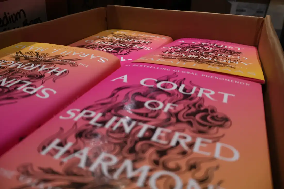 A box filled with pink and yellow hardcover books titled “A Broken Court of Harmony.”