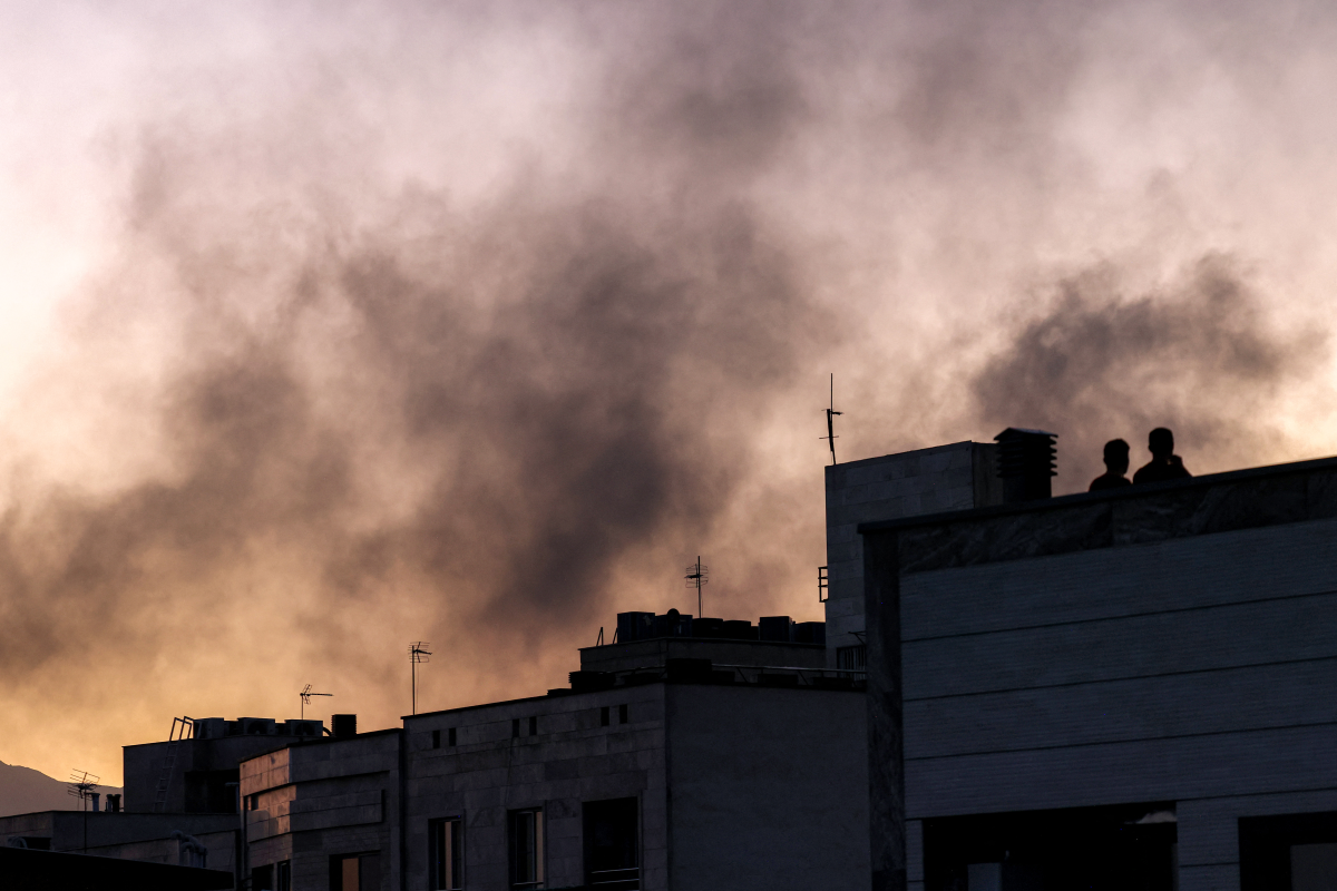 People stand on a rooftop amidst billowing smoke following an overinght Israeli strike in Tehran on June 17, 2025.