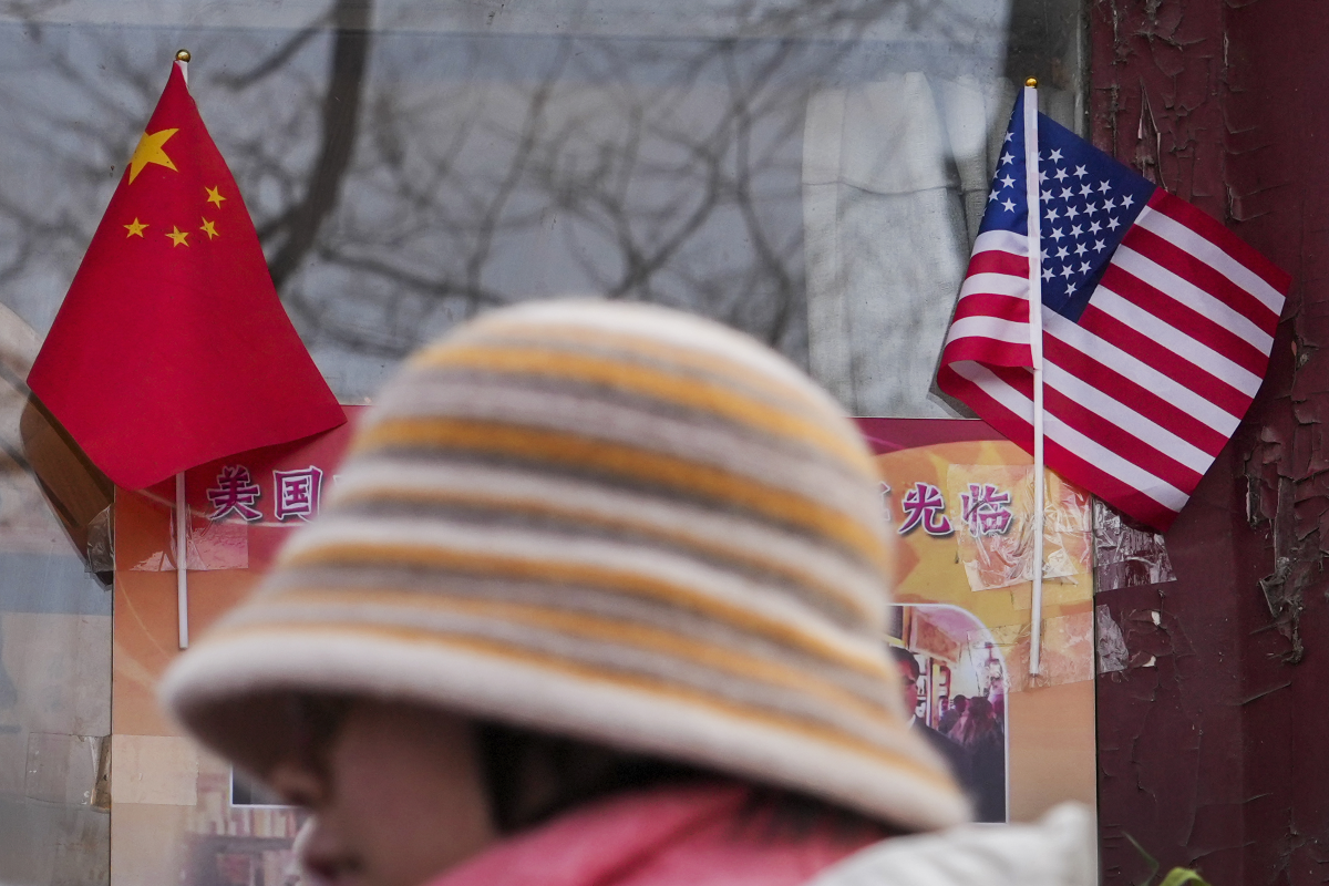 A woman walks by the Chinese and U.S. national flags on display outside a souvenir shop in Beijing on Jan. 31, 2025. Both China and the U.S. are taking ever more assertive measures as they vie for leadership in key technologies from artificial intelligence and semiconductors to electric vehicle batteries.