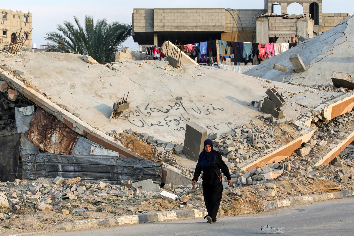 A woman walks past the rubble of a collapsed building at a camp for people displaced by conflict in Bureij, in the central Gaza Strip, on Jan. 17, following the announcement of a truce amid the war between Israel and Hamas.