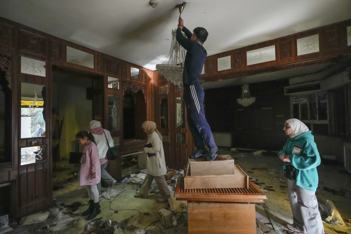 A man tries to take a lamp as people search for belongings in the ransacked private residence of Syrian President Bashar Assad in the Malkeh district of Damascus, Syria, on Sunday.