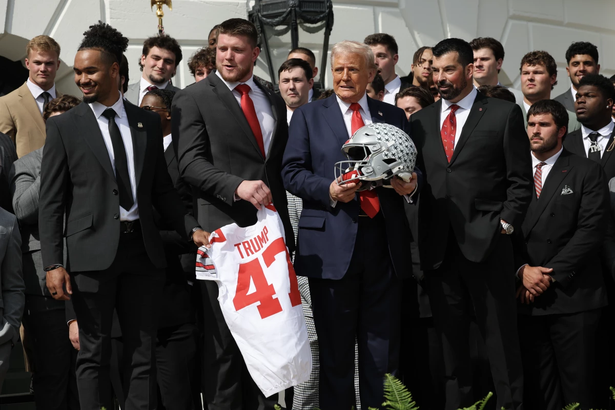 President Trump stands with Ohio State Head Coach Ryan Day (R) as he welcomed the 2025 College Football National Champions from Ohio State University to the White House during a ceremony on April 14, 2025 in Washington, DC. Trump's new executive order seeks to ban 'pay-for-play' deals and requires schools to provide scholarships in women's and Olympic sports — and it dangles the threat of withholding federal funds to schools as an enforcement mechanism.