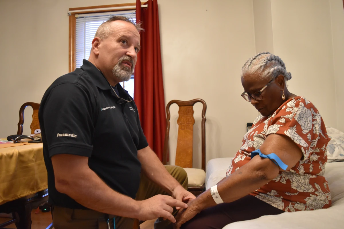 Shane McMahon, a paramedic, checks on Stephanie Joseph, 91, who received care through Mass General Brigham's hospital-at-home program.