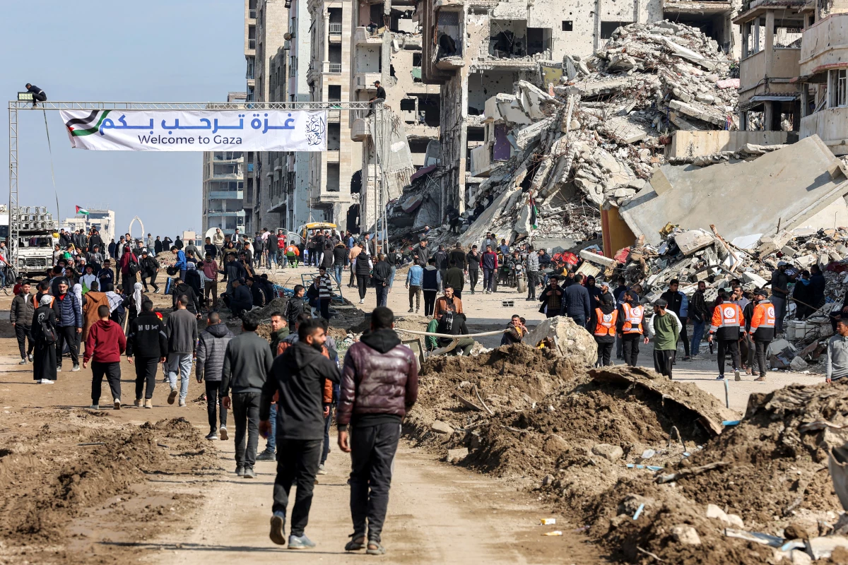 People gather by a banner welcoming people near the rubble of a collapsed building along Gaza's coastal al-Rashid Street for people to cross from the Israeli-blocked Netzarim corridor from the southern Gaza Strip into Gaza City on Sunday.