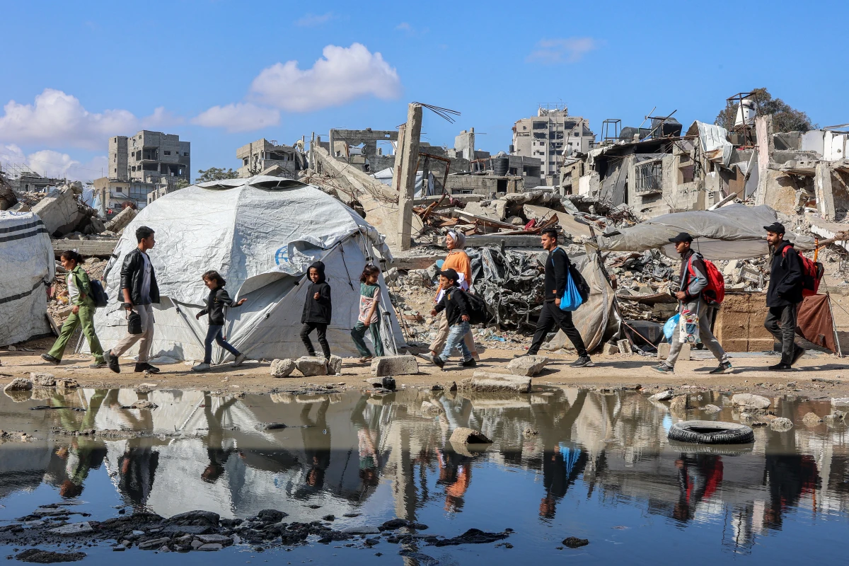 People walk by a tent shelter near the rubble of a collapsed building in western Gaza City on April 15.