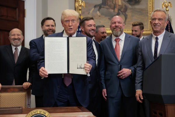 Trump displays a signed executive order, surrounded by officials and pro athletes.
