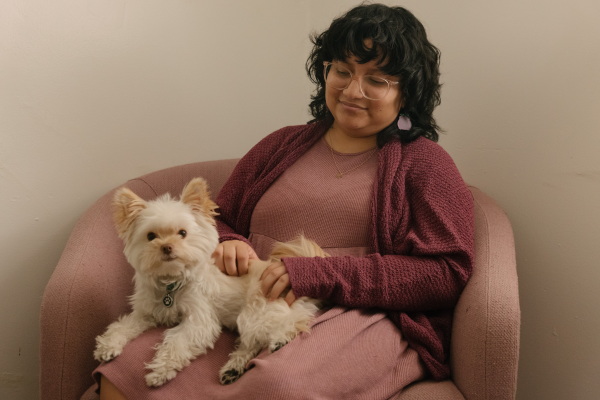 Lourdes Monje sits with a small white dog named Tofu in their lap.