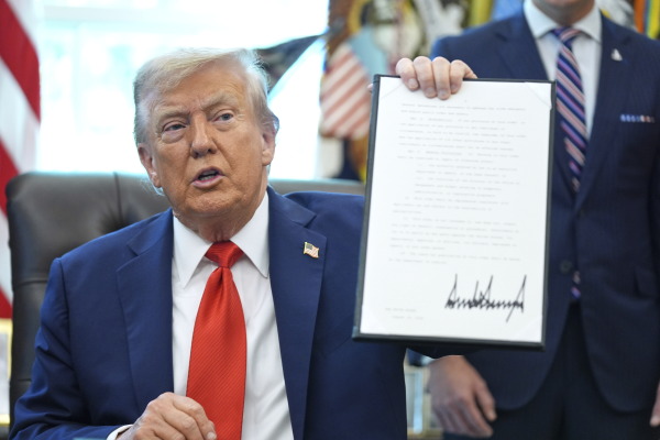 President Trump holds up a signed executive order requiring the Justice Department to investigate instances of flag burning, in the Oval Office of the White House on Monday.