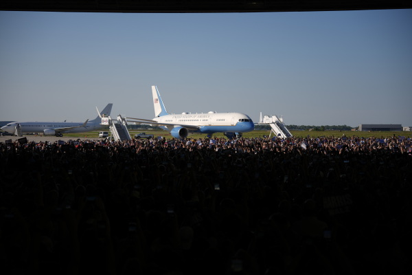 This photo shows Air Force Two at the Harris campaign rally in Detroit on Aug. 7. The background shows a light blue sky. The foreground shows a crowd of people as well as areas that are too dark to see individual people.