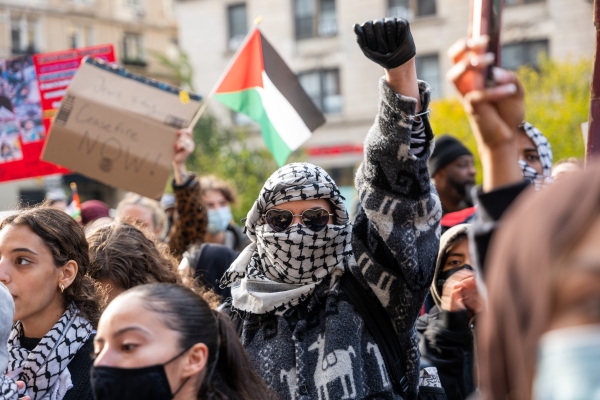This photo shows a crowd of students taking part in pro-Palestinian protests in November. Some are wearing keffiyehs. Some are holding signs. The student in the middle is holding a fist in the air.