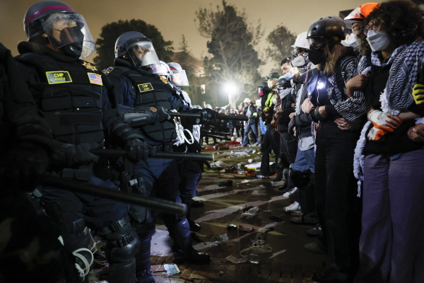 This photo shows police and pro-Palestinian students facing off at the University of California, Los Angeles in May. A row of police officers wearing riot gear stands on the left, and a few feet across from them on the right stands a row of pro-Palestinian students with arms locked together.