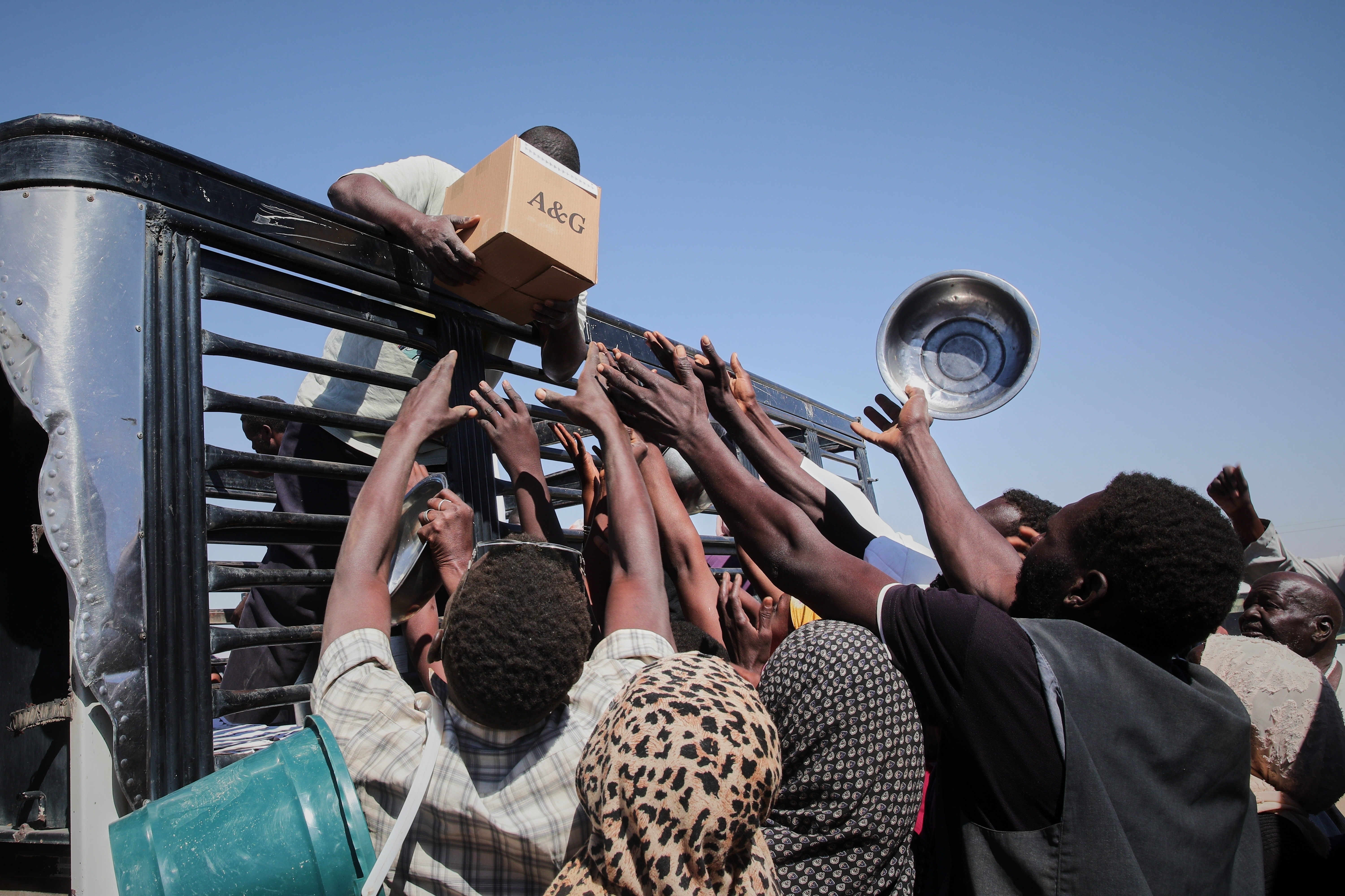 Sudanese families displaced from El-Fasher reach out as aid workers distribute food supplies at the newly established El-Afadh camp in Al Dabbah, in Sudan's Northern State, Sunday, Nov. 16, 2025.