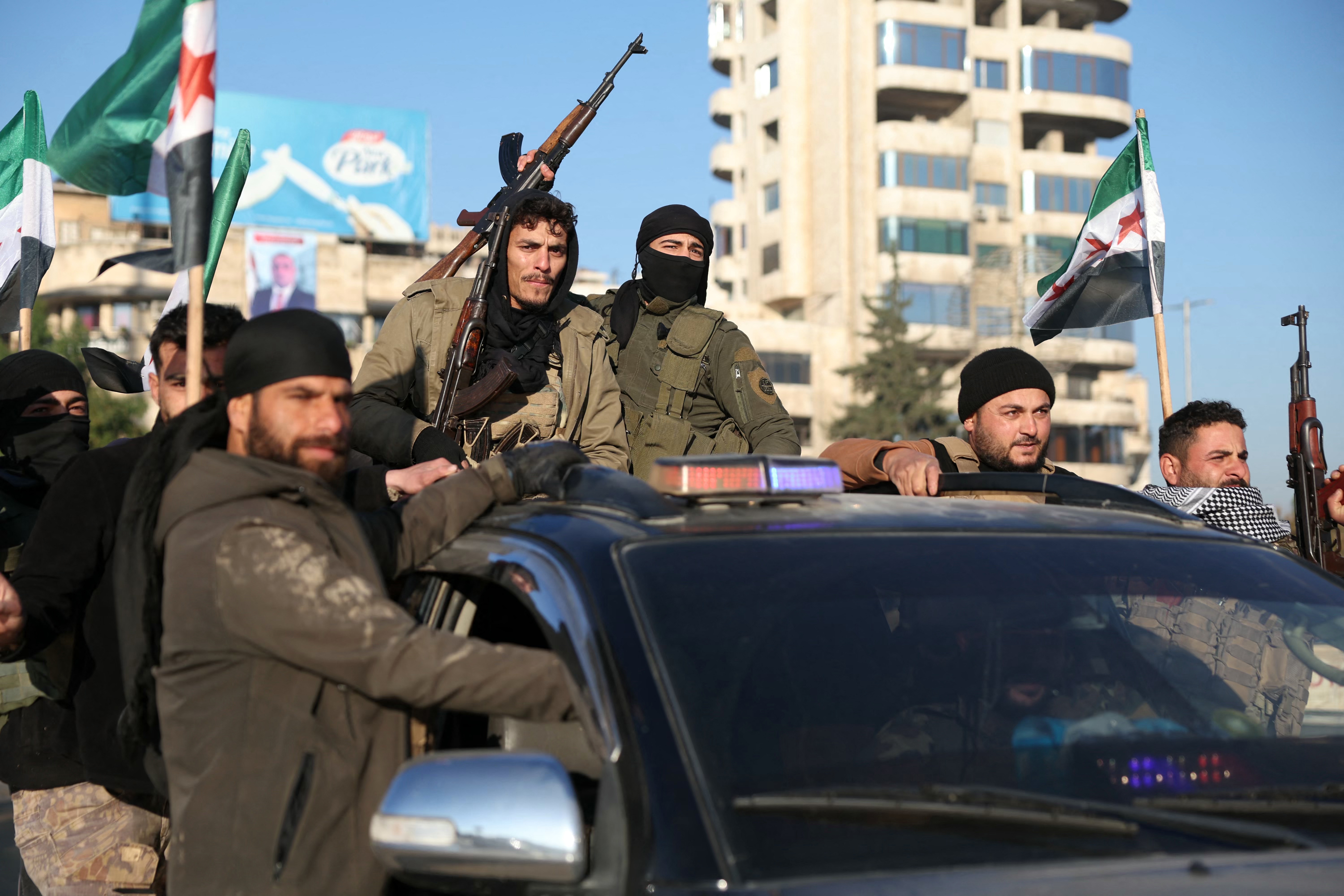 Antigovernment fighters brandish their guns as they ride a vehicle in Syria