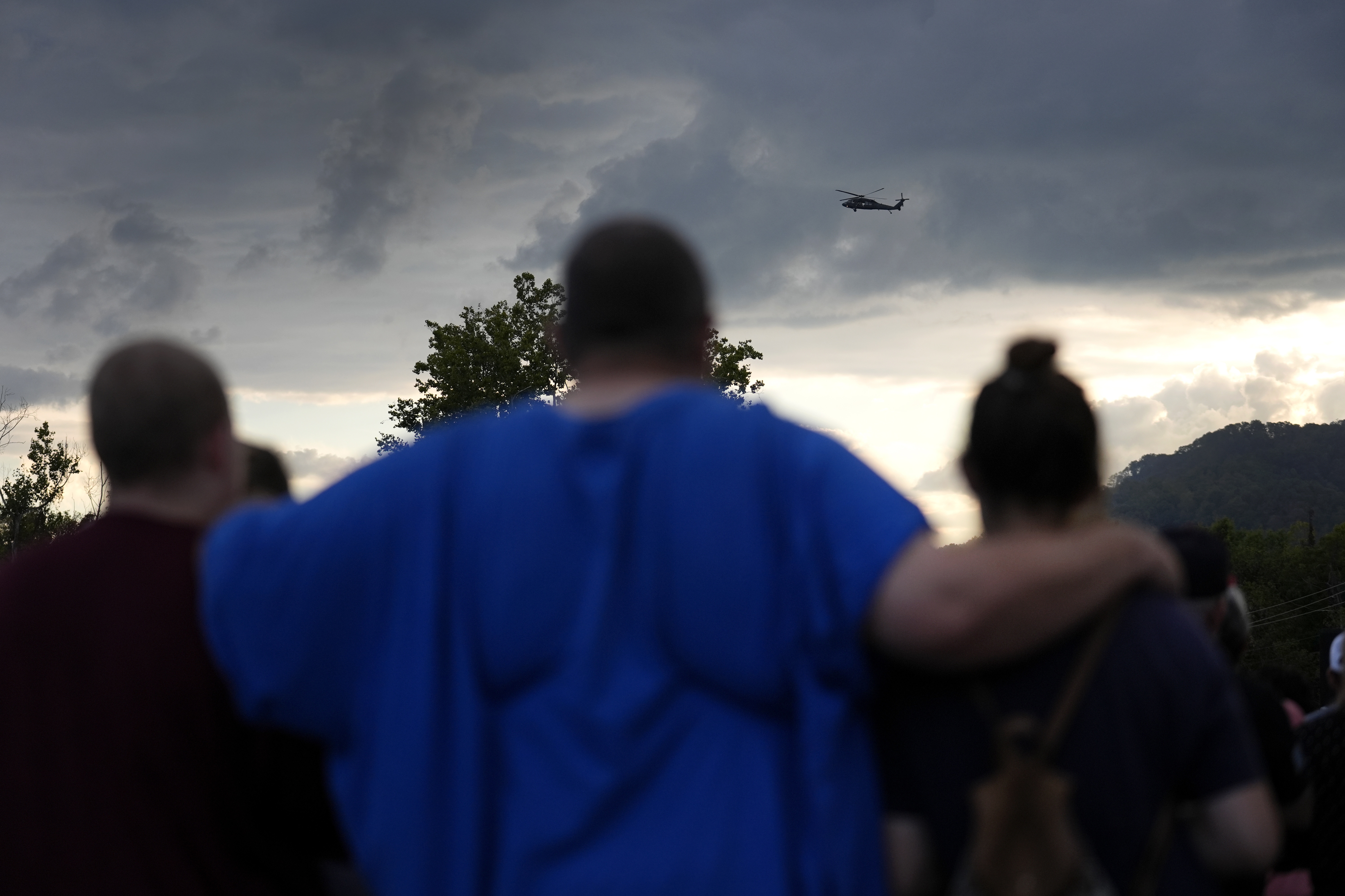 Mourners gather during a vigil for victims of the Impact Plastics flooding as a helicopter continues search and rescue work in Erwin, Tenn., on Oct. 3.