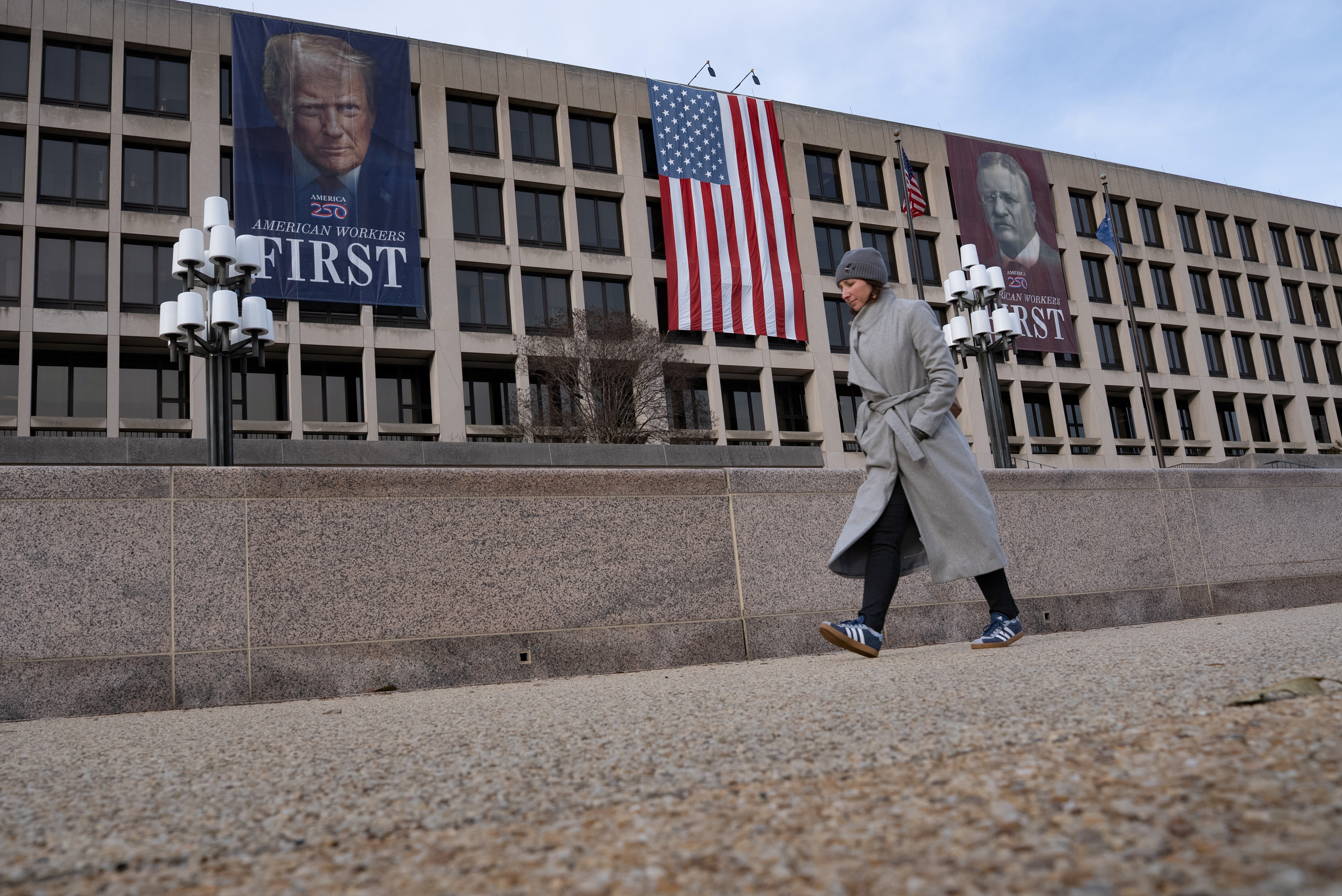 A person walks by a banner depicting President Trump on the face of the Labor Department building near the Capitol in Washington, DC in February 2026