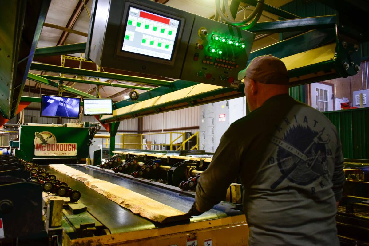 An employee at GreenTree Forest Products feeds a rough cut board into a special machine that trims the bark edge off to reduce any scrap product at the mill.