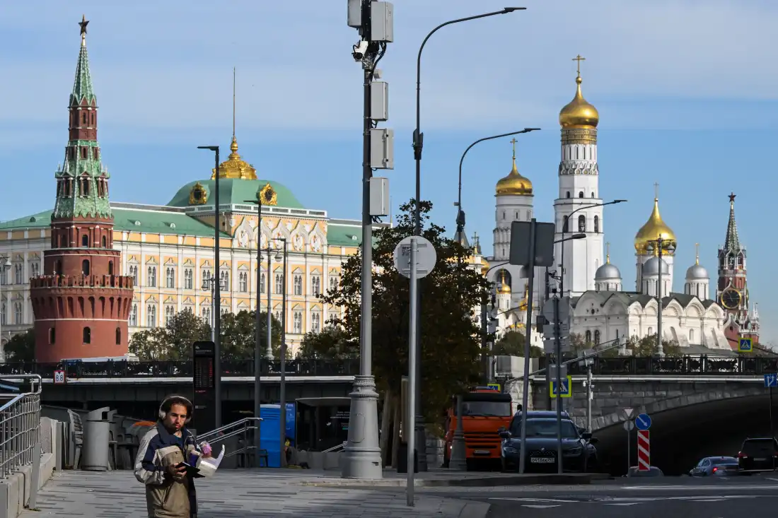 A pedestrian looks at his smartphone on an embankment with the Kremlin in the background in central Moscow on October 8, 2026. Researchers who track online influence operations say Kremlin-backed groups are renewing tactics they’ve used to sow distrust and discord in previous elections in the U.S. and around the world.
