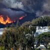 A raging fire behind a row of houses sends up dark smoke.