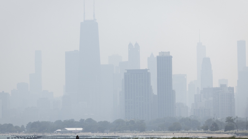 People sun tan in grass off the Lakefront Trail on the North Side as a haze of Canadian wildfire smoke blankets the Chicago area and creates poor air quality, Thursday, July 31, 2025.