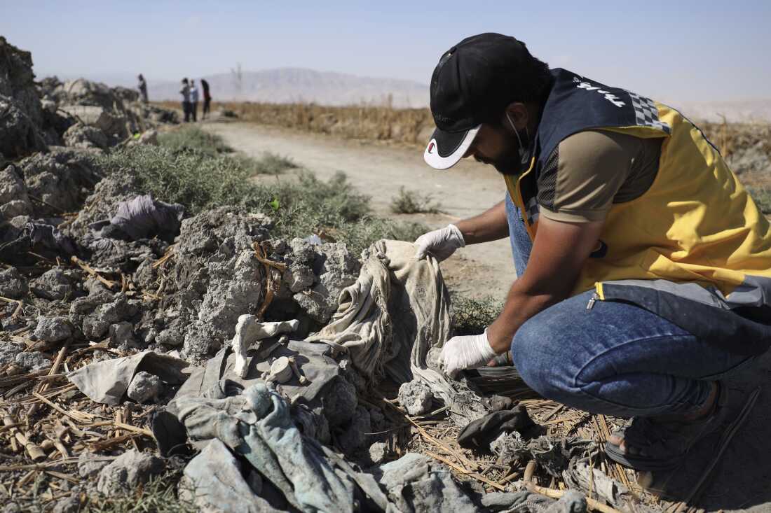A Syrian Civil Defense worker checks clothes found along with human remains in Otaiba, on the outskirts of Damascus, Syria, Sept. 19.