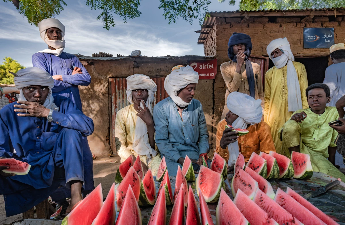 Young men eat slices of watermelon at a vendor's stall in a market in the village of Karnak, Chad. The village has seen Great Green Wall interventions from an nongovernmental group looking to plant acacia trees.