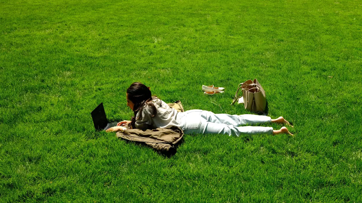 A woman uses a laptop as she lies on the grass in a park in the Manhattan borough of New York City on April 24, 2026.
