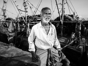 Nandu Kumar, 65, sits among fishing boats at Kasimedu Fishing Harbour in Chennai, India. A former fisherman who now sells fish on shore, Kumar says he once smuggled imported alcohol and cigarettes to make a living.
