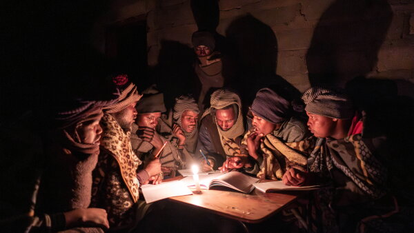 A group of people sitting around a table with a book, some papers and a candlelight.