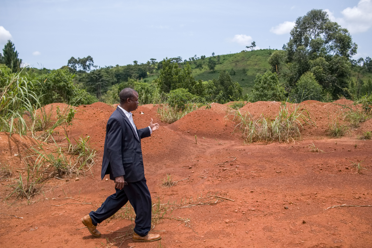 Bassima Joram received more than $30,000 for his land — significantly more than many of his neighbors. But he maintains it wasn't nearly enough to replace what he lost. Here he walks past abandoned hips of murram and waste that has polluted natural water sources in Kabale village.