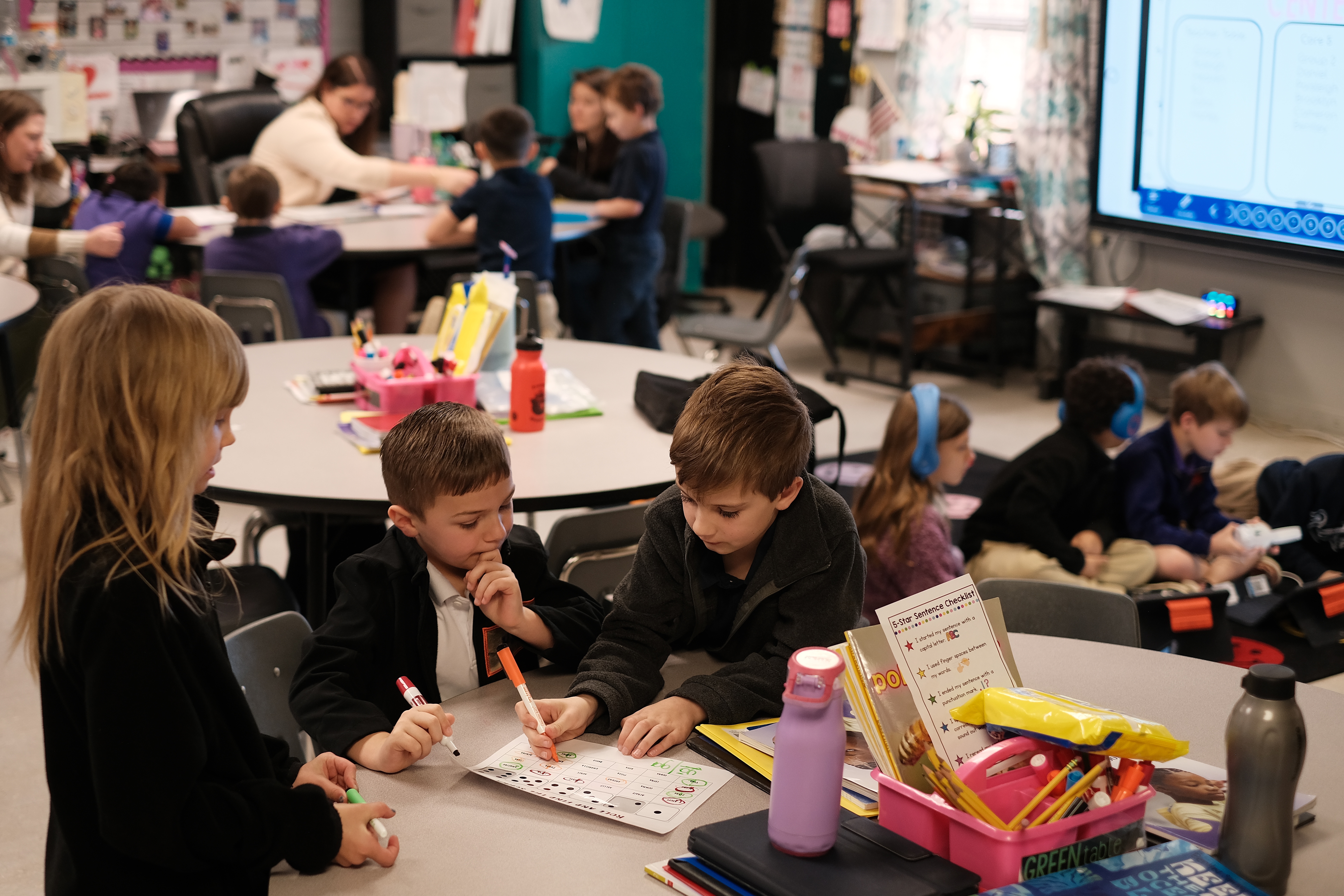 Second graders Serena Lacour, Luke Busby and Dylan Poche work on a word-identification reading game, while other groups work with their teacher, Cady Caskey, on sounding out words. (NPR)