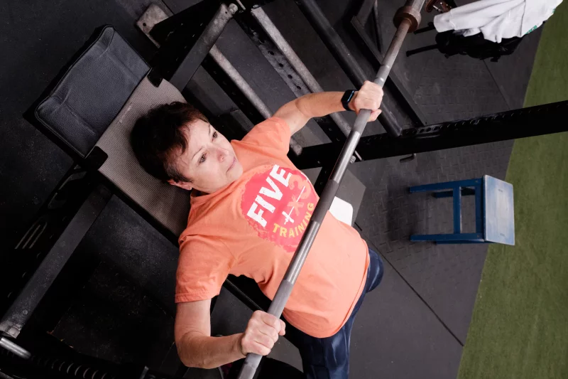 A young couple stands‌ smiling in front of their tiny home, surrounded by greenery.