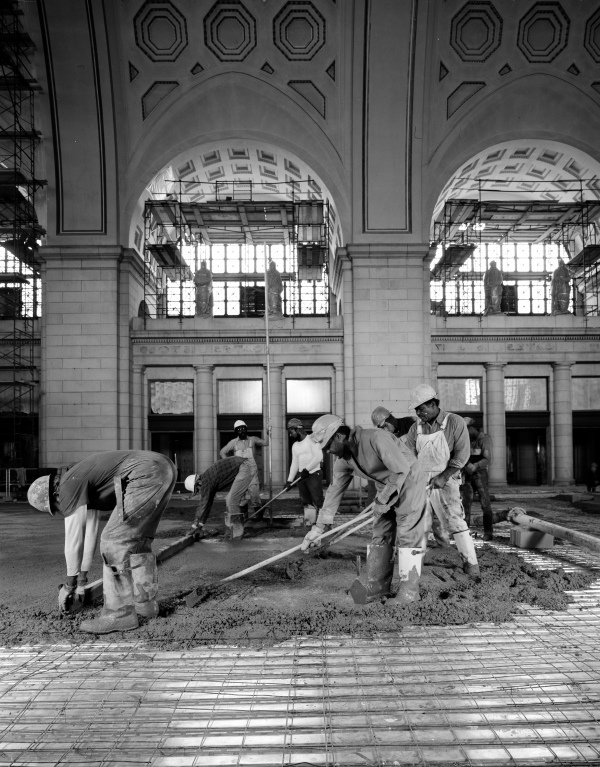 In this black-and-white photo, workers wearing boots and hard hats work with cement during the 1980s restoration of Union Station.
