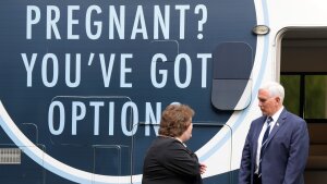 Former VP Mike Pence and Alexa Newman stand next to an RV that has an enormous sign that says, "Pregnant? You've got options."
