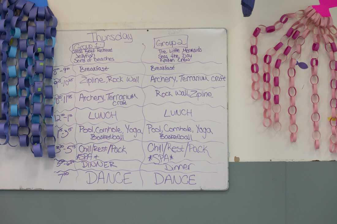 A whiteboard hanging on a wall at Camp Cranium displays the day's schedule for campers, which includes activities such as a zip line, archery, a rock wall, yoga and a dance.