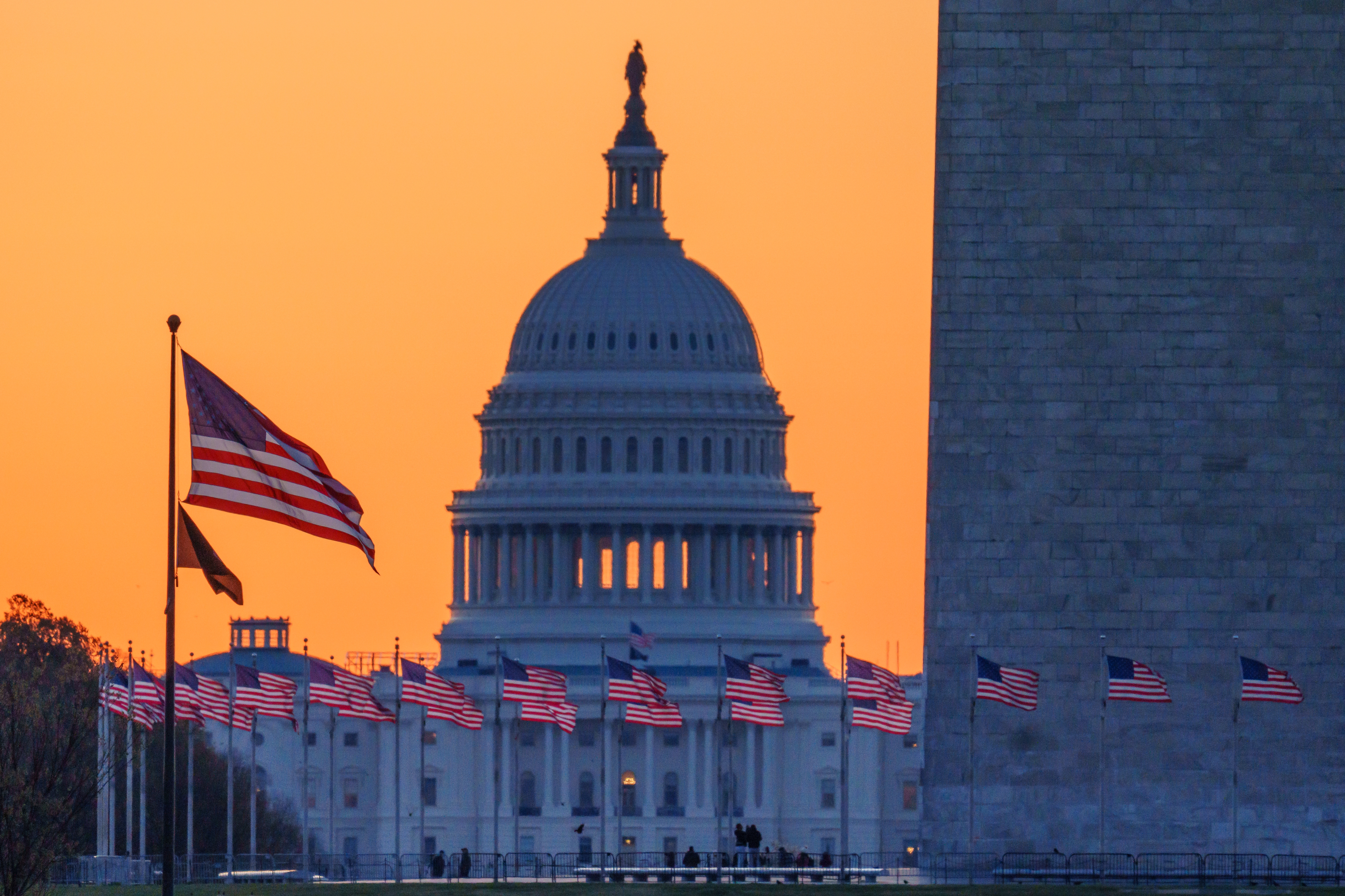 Sunrise turns the sky orange behind the U.S. Capitol building as it illuminates the U.S. flags circling the base of the Washington Monument on March 23 in Washington, D.C.