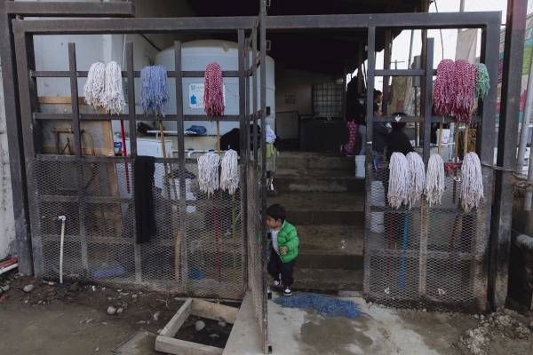 A child peers through the gate doors as women wash clothes at the Embajadores de Jesús church in Tijuana, Mexico, on Dec. 6, 2024. Zaydee Sanchez for NPR